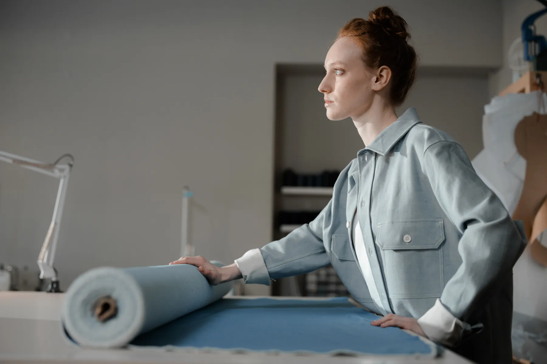 A maker rolling out cloth across a cutting table in a daylit workroom