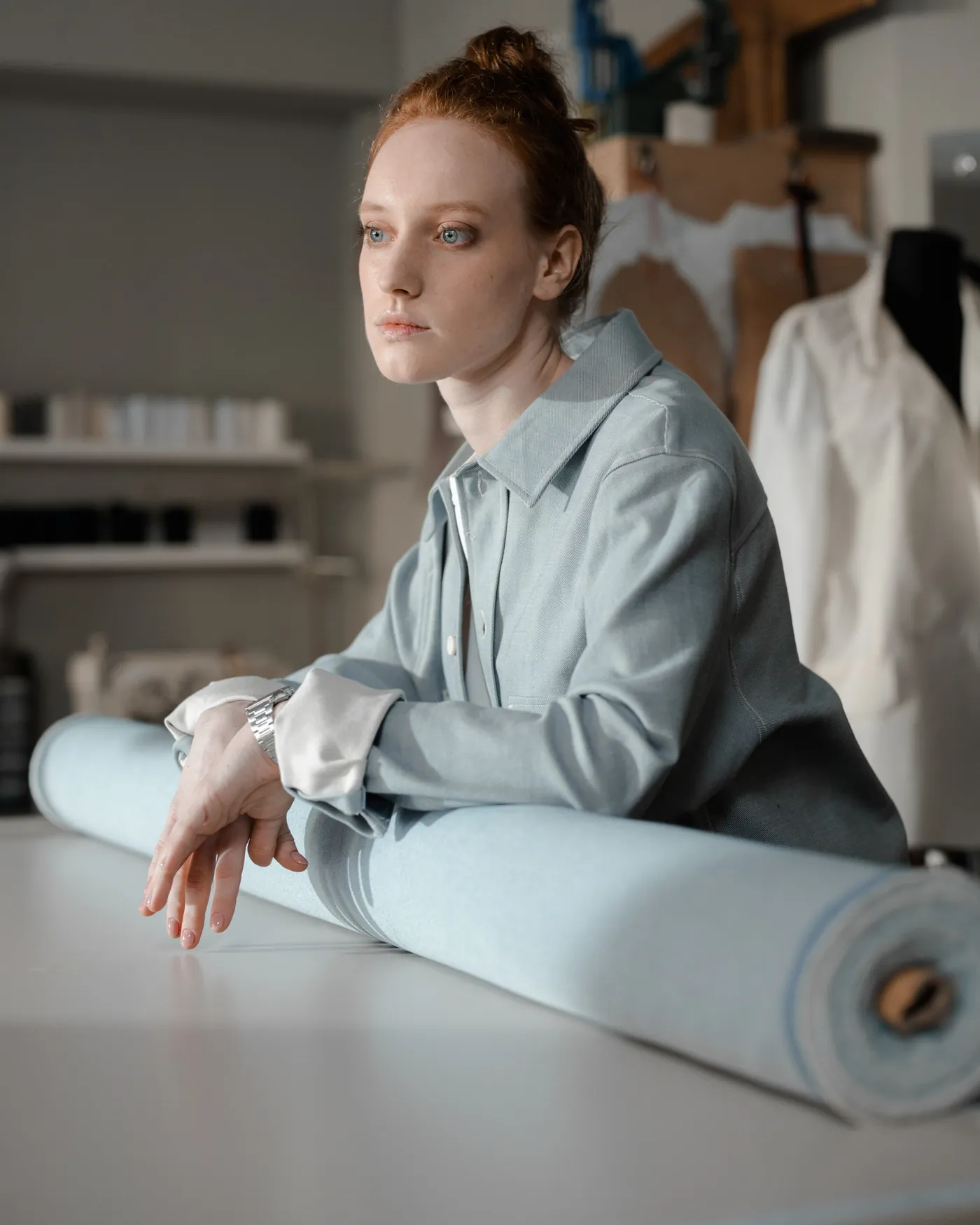 A maker resting on a bolt of cloth at a cutting table in a daylit workroom