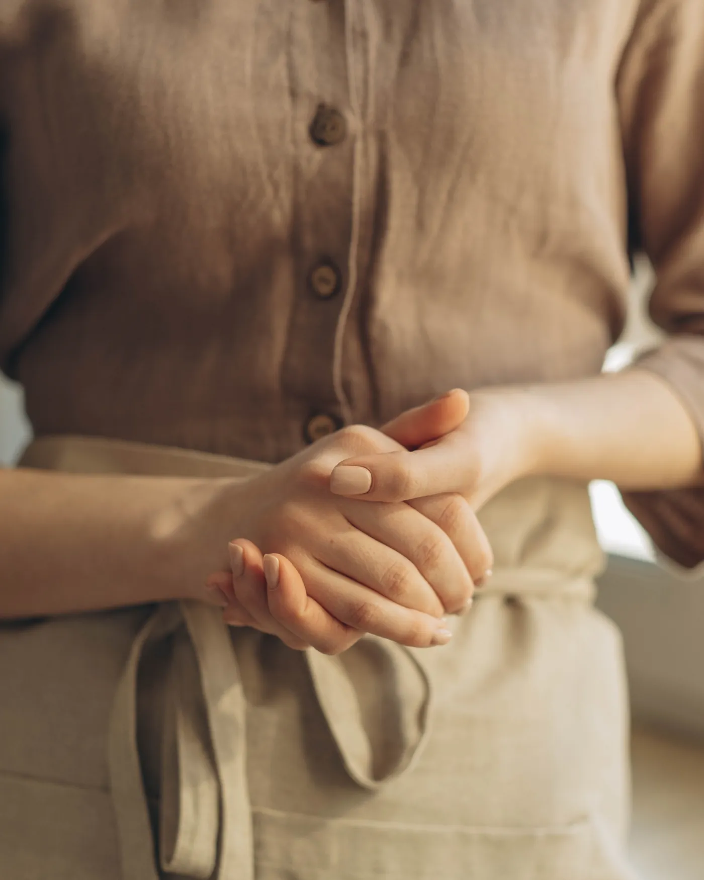 Hands folded over a linen apron, photographed close in warm daylight