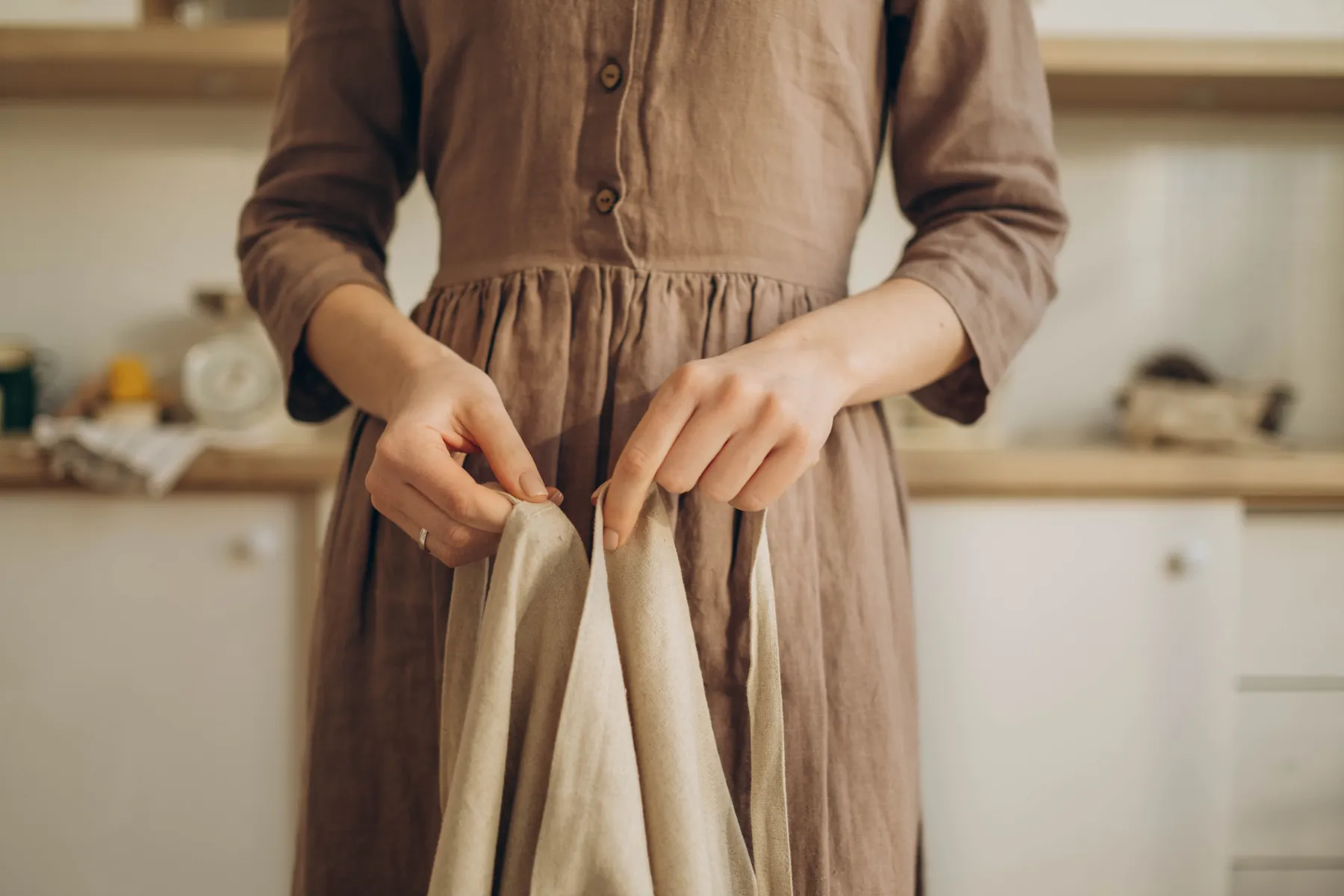 A linen dress held open by two hands in a bright workroom