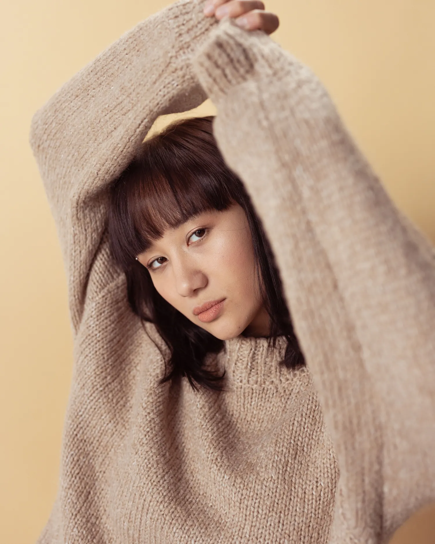 Mere Knit — Model raising the sleeves of an oatmeal hand-knitted sweater