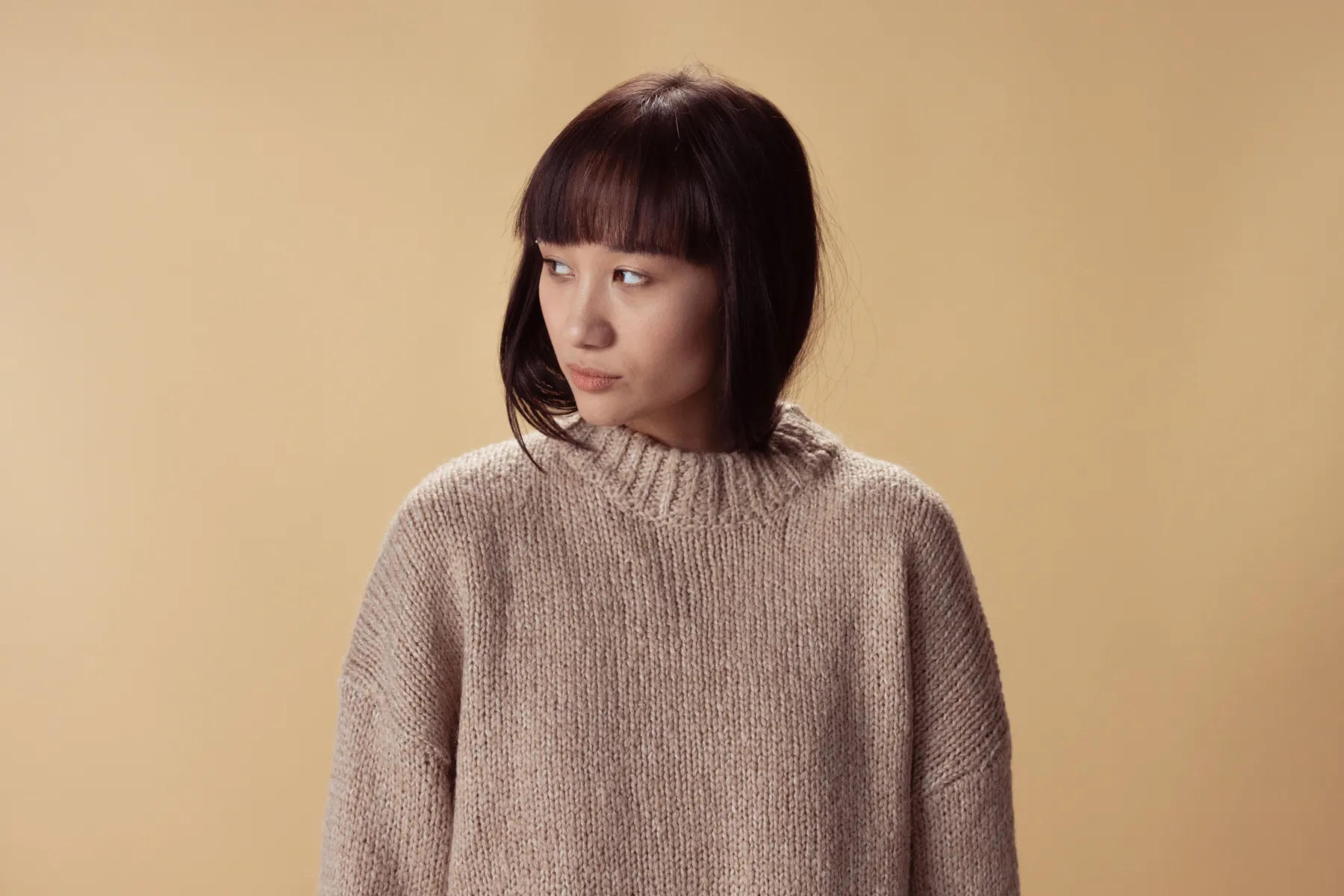 Model seated in an oatmeal hand-knitted sweater, photographed wide