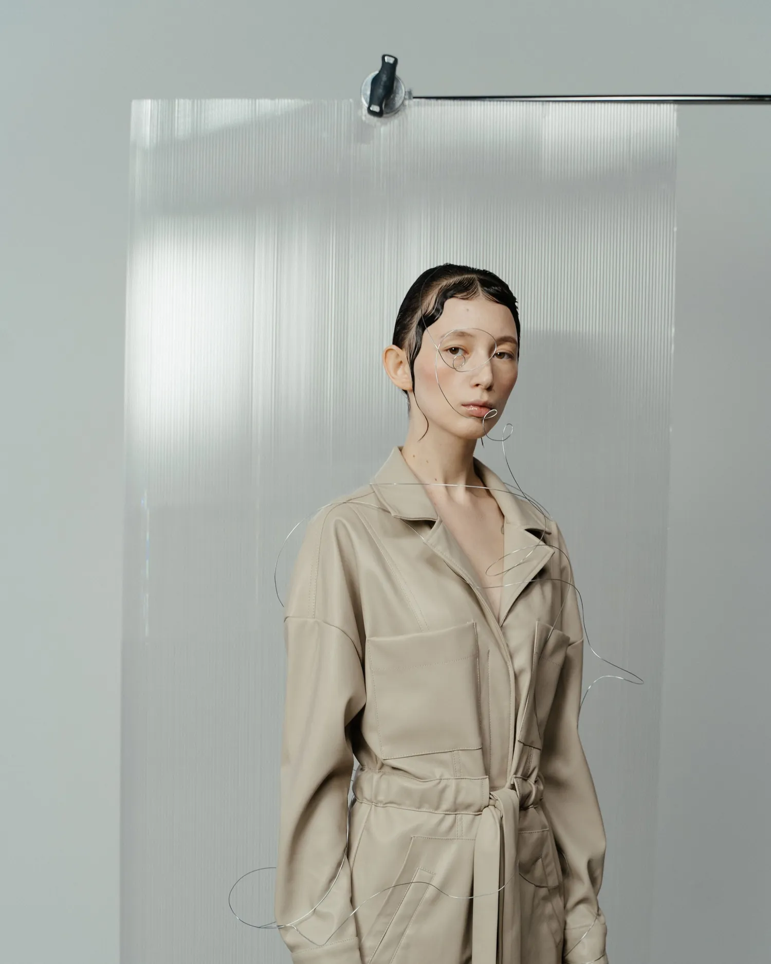 Model in a sand linen overall standing in front of fluted glass