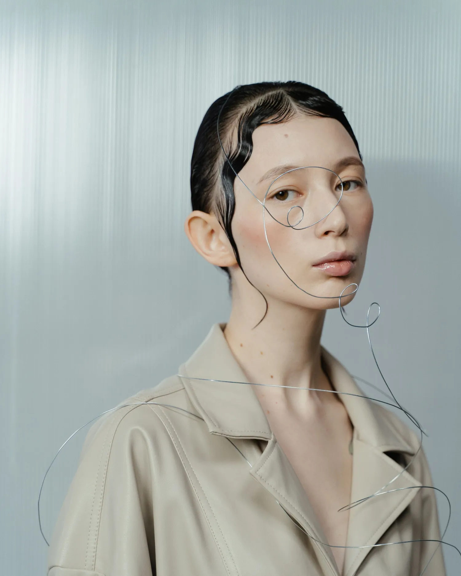 Model in a sand linen overall seen through fluted glass, hand raised
