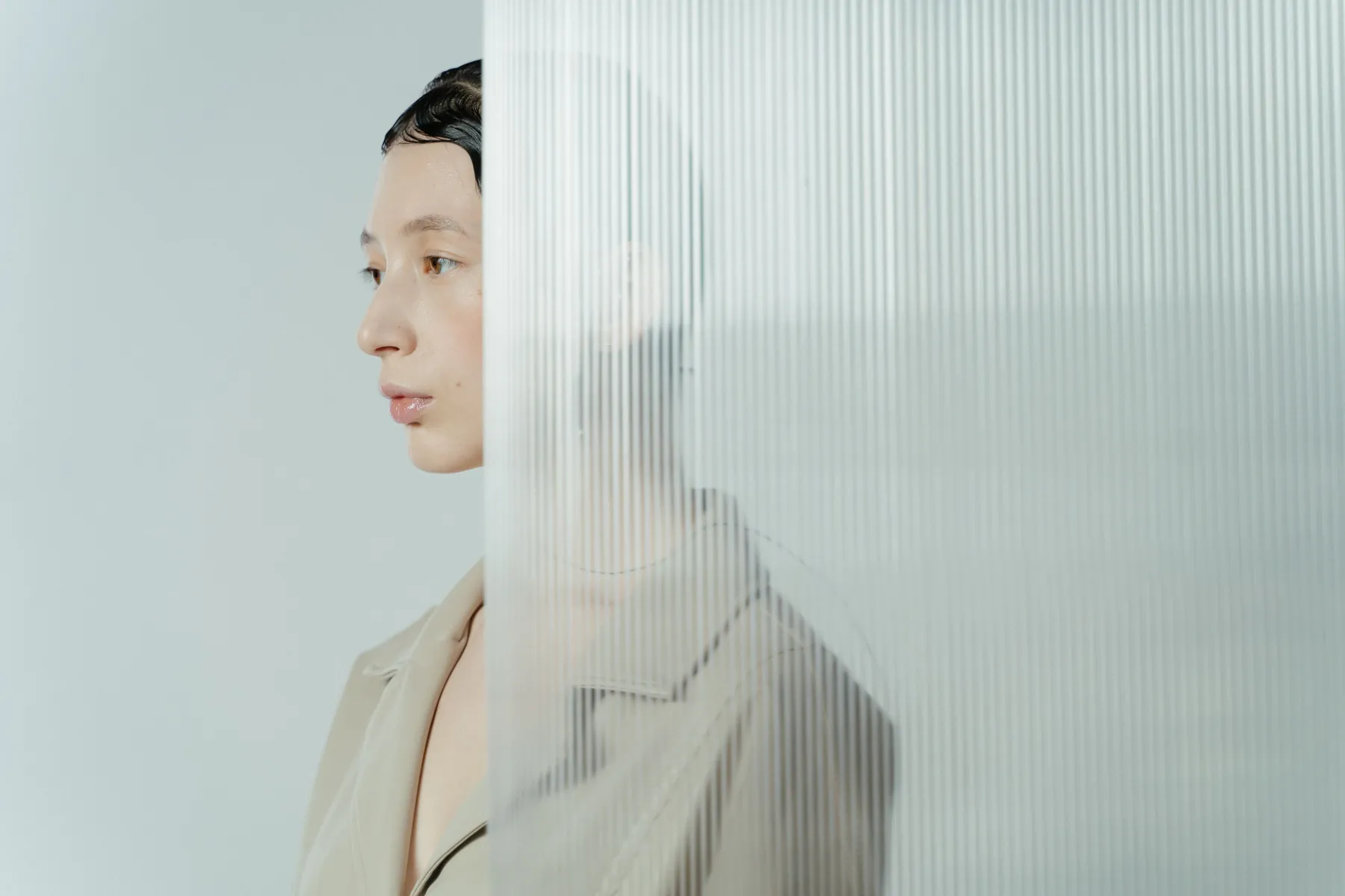 Profile of a model in a sand linen overall beside fluted glass