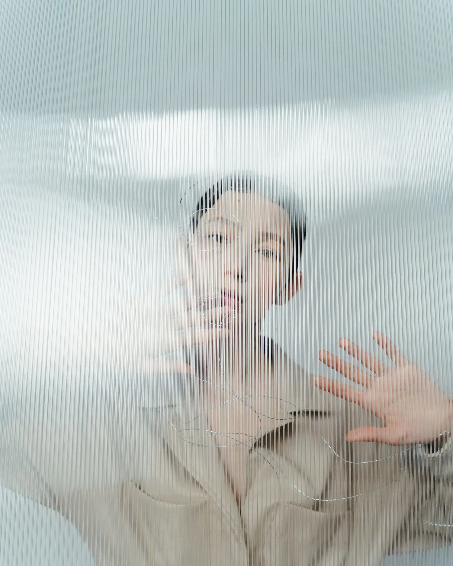 Model in a sand linen overall almost hidden behind fluted glass