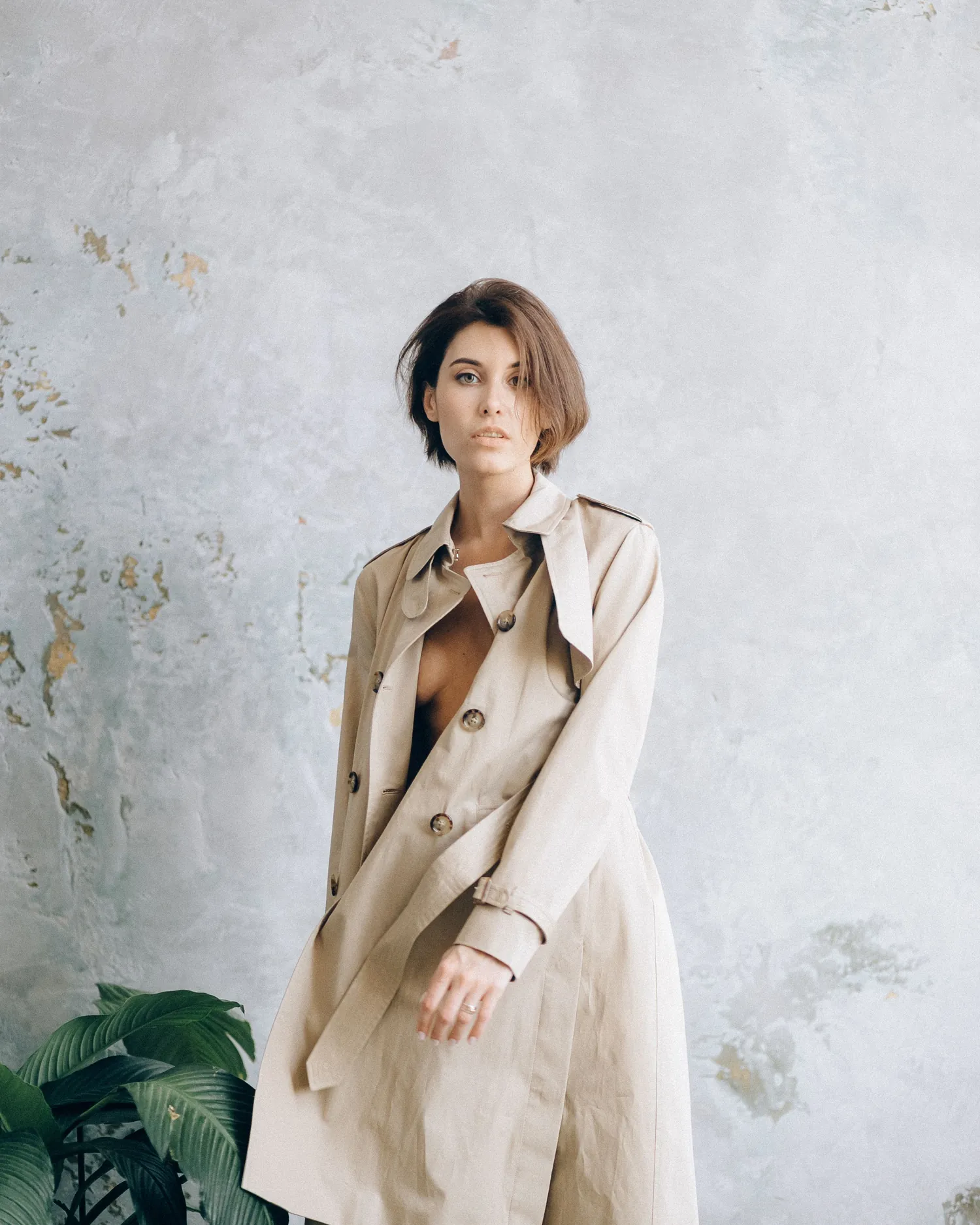 Model wearing a sand linen long coat against a plaster wall