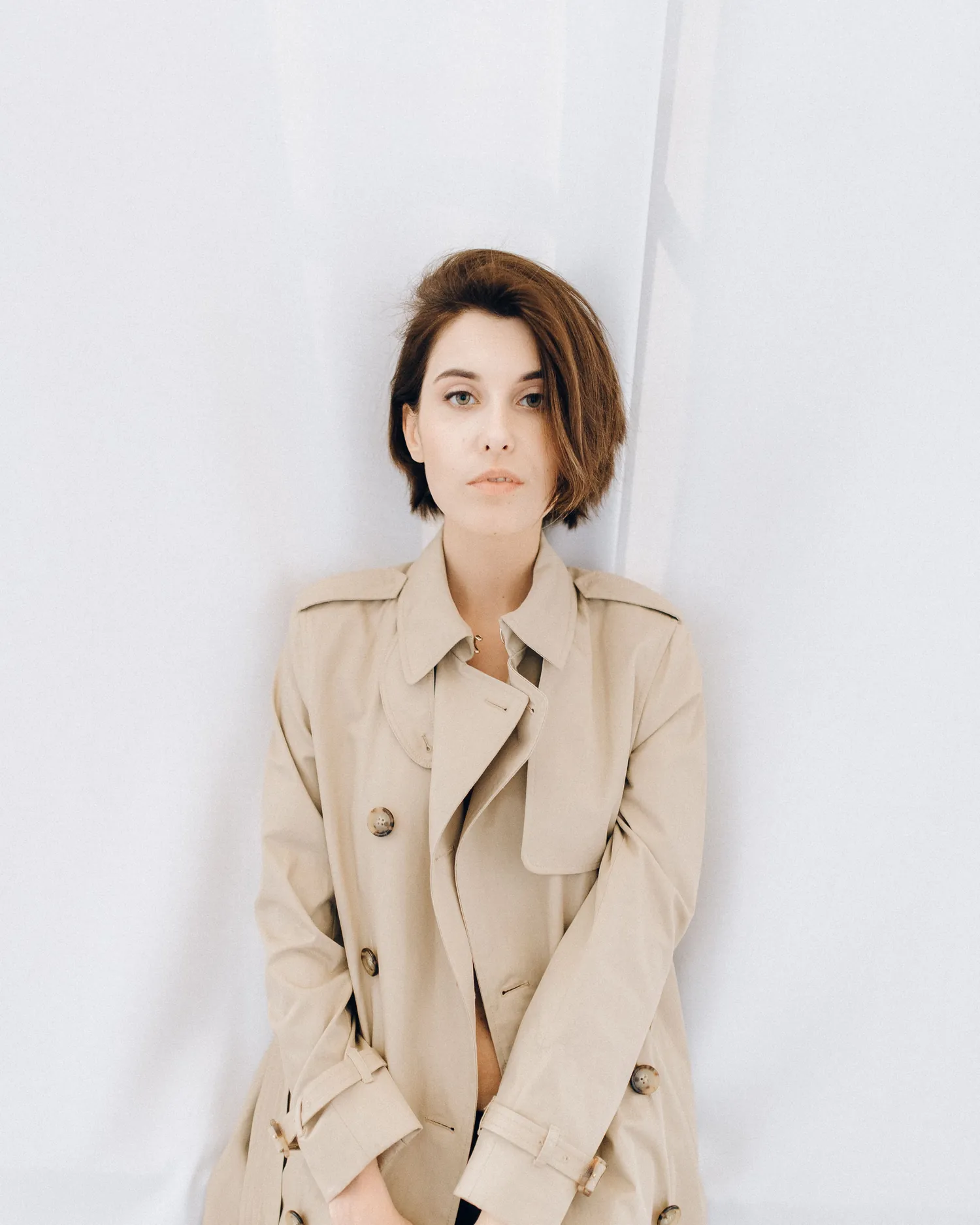 The Short Coat — Model wearing a sand linen short coat against a white curtain