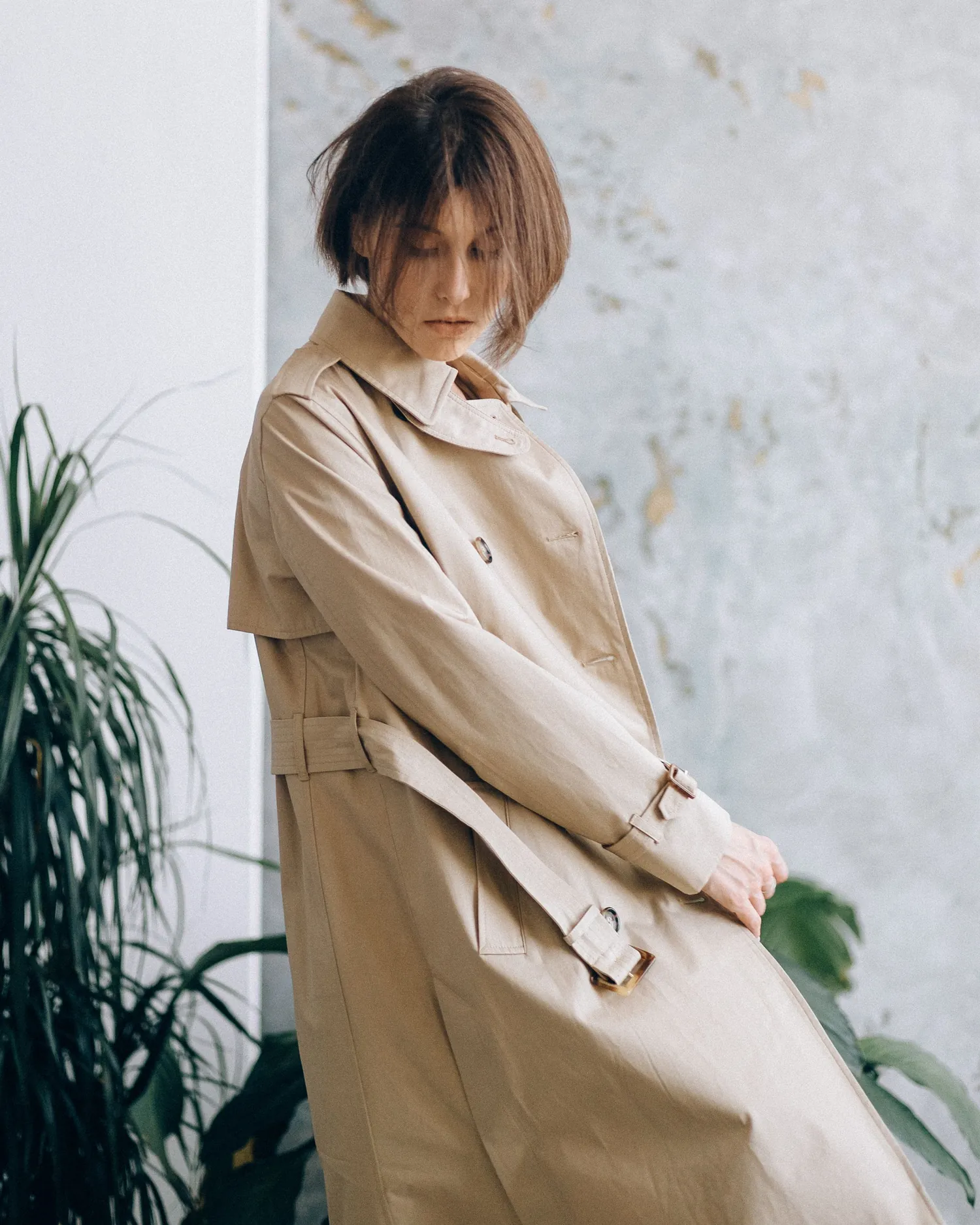 Sand linen long coat photographed in profile beside a plant