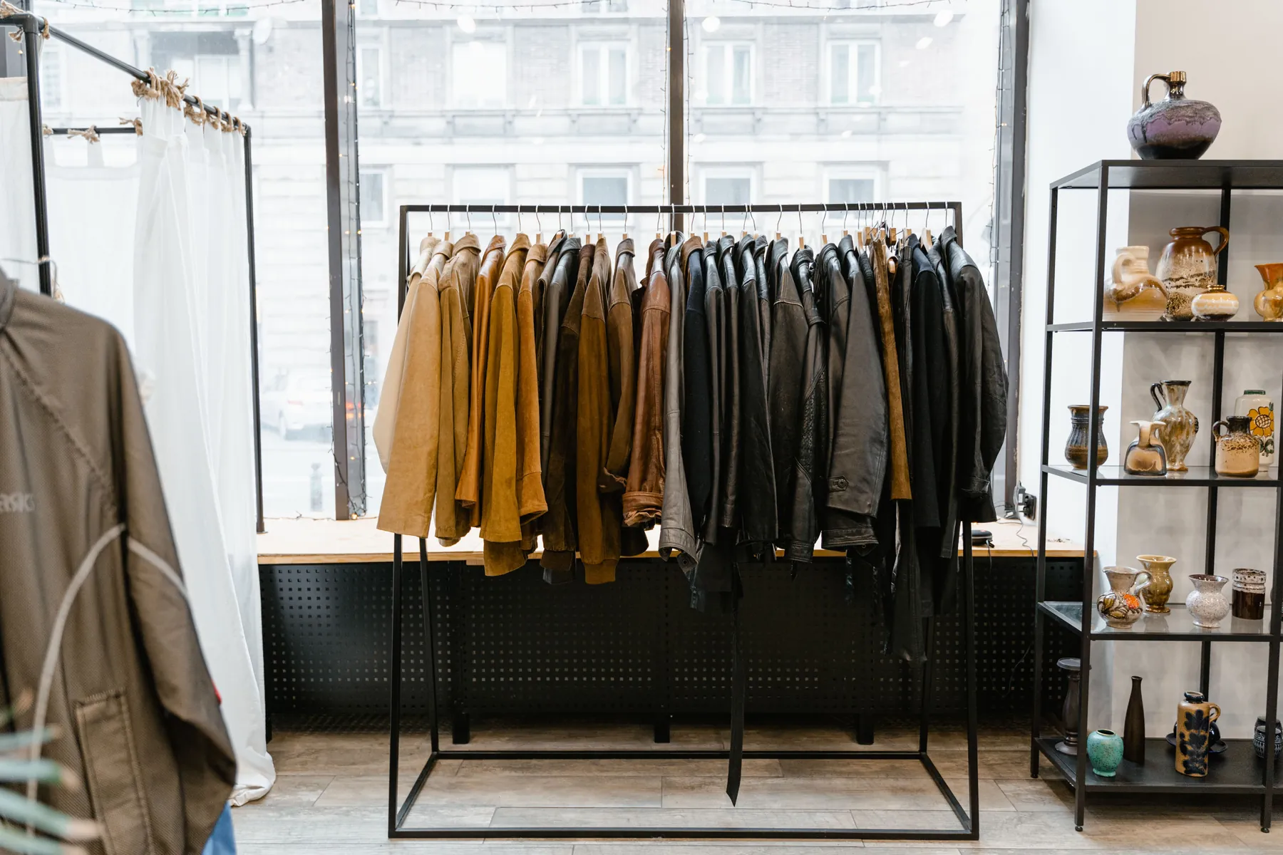 A minimal store interior with jackets hung on a black rail by a window
